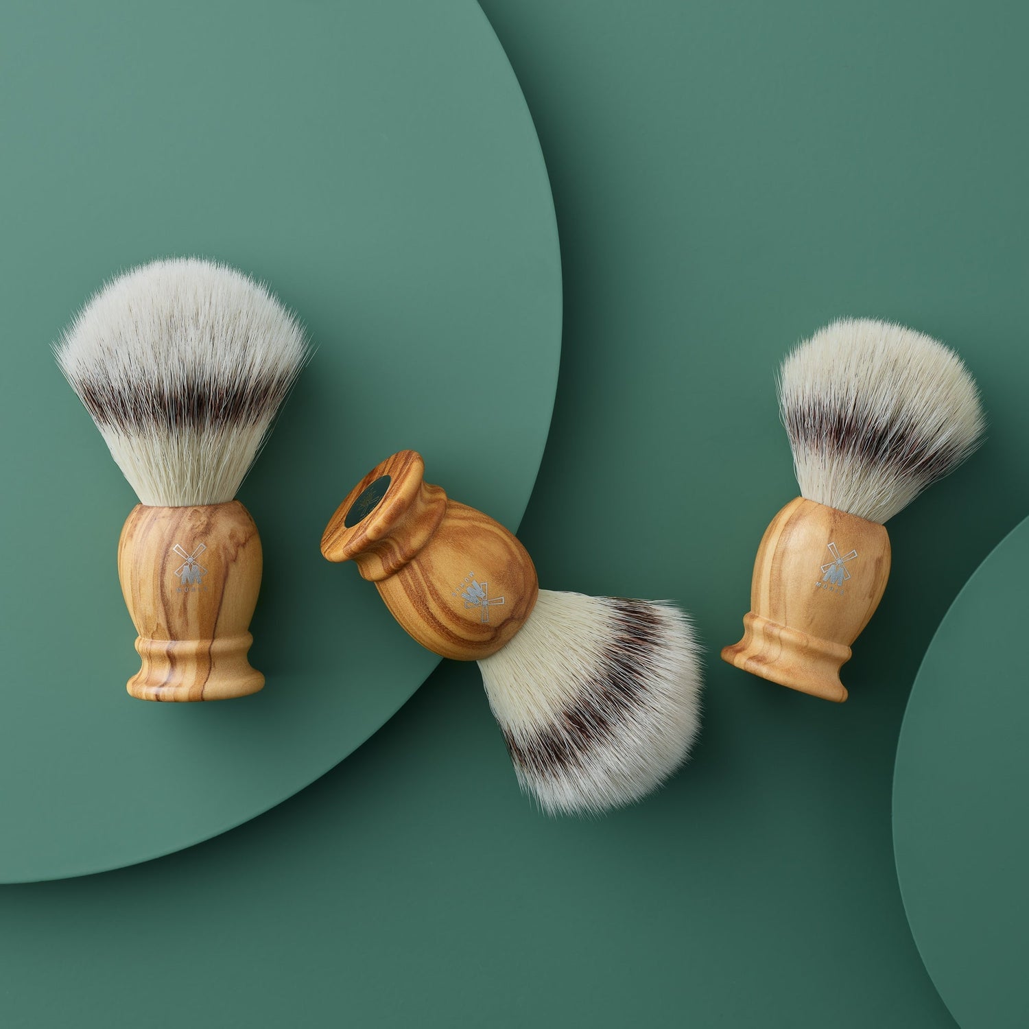 Tre eksklusive barberkoste med træskaft og tætte børstehår i høj kvalitet, opstillet på dekorativ baggrund – illustration af forskellige typer barberkost til guide om valg af den rette barberkost.
