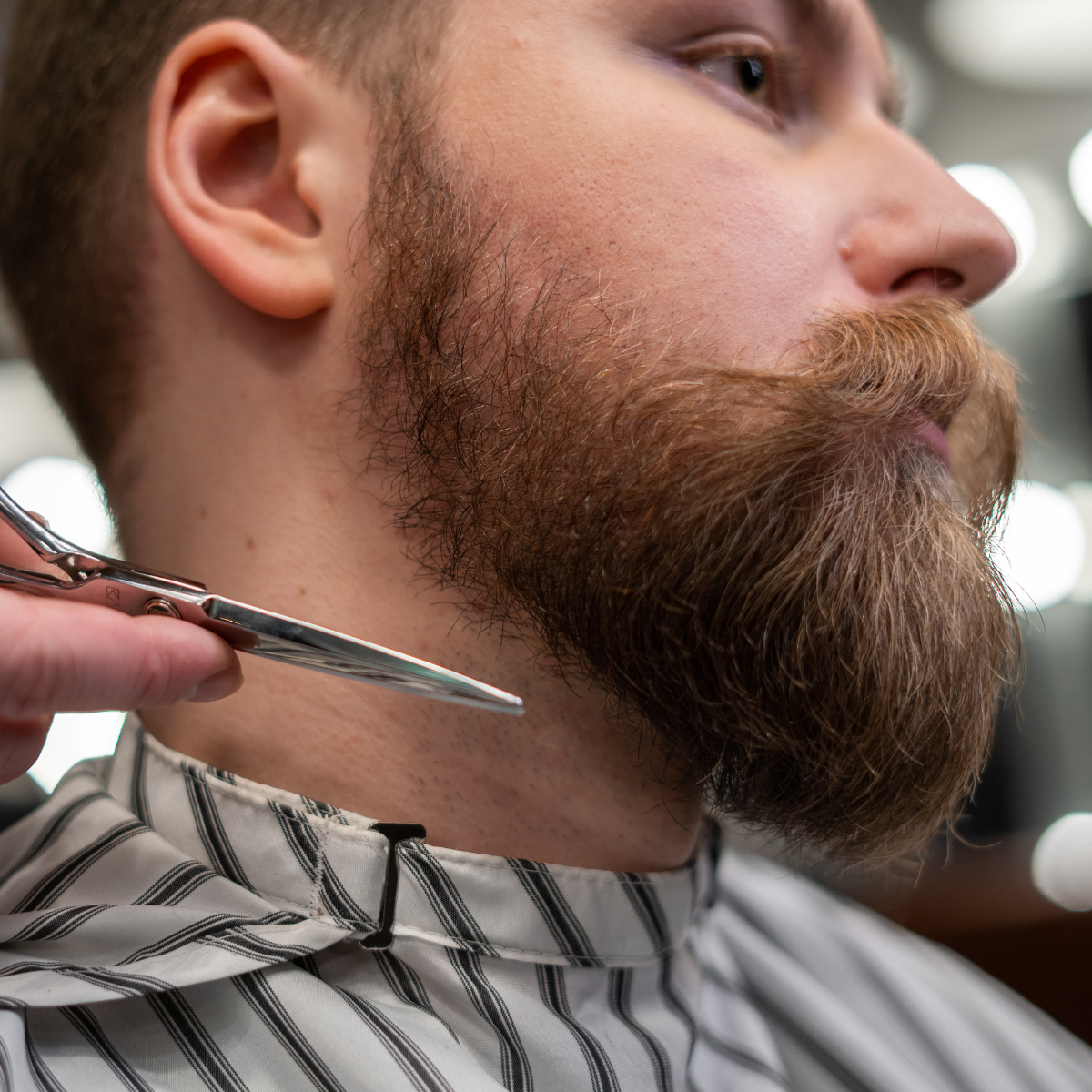 Mand tæmmer og trimmer fuldskæg med saks i barbersalon – skægpleje og grooming for et velsoigneret look